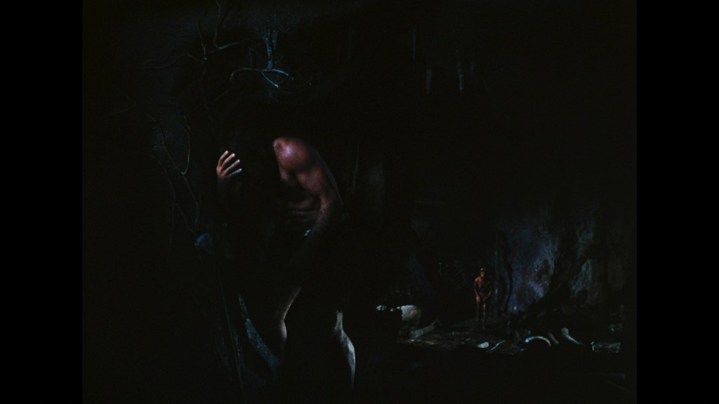 A dimly lit cave scene featuring a muscular figure clutching their head in distress, with another smaller figure in the background. The environment includes dark shadows and textured surfaces.