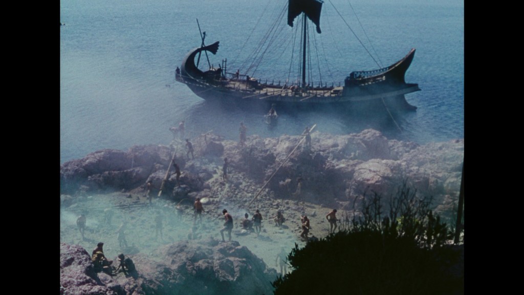 A vintage ship sailing in the ocean with rocky shorelines and several people working on the beach, creating a scene of exploration or adventure.