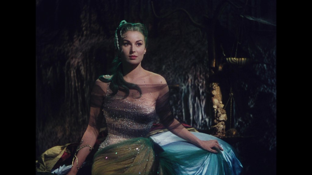 A woman with long hair wearing a sparkling, sheer dress sits elegantly in a dimly lit setting, showcasing a mysterious and captivating expression.