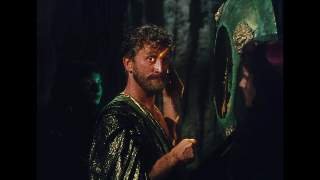 A man with a beard in a robe looking into a mystical mirror, with shadowy figures in the background.