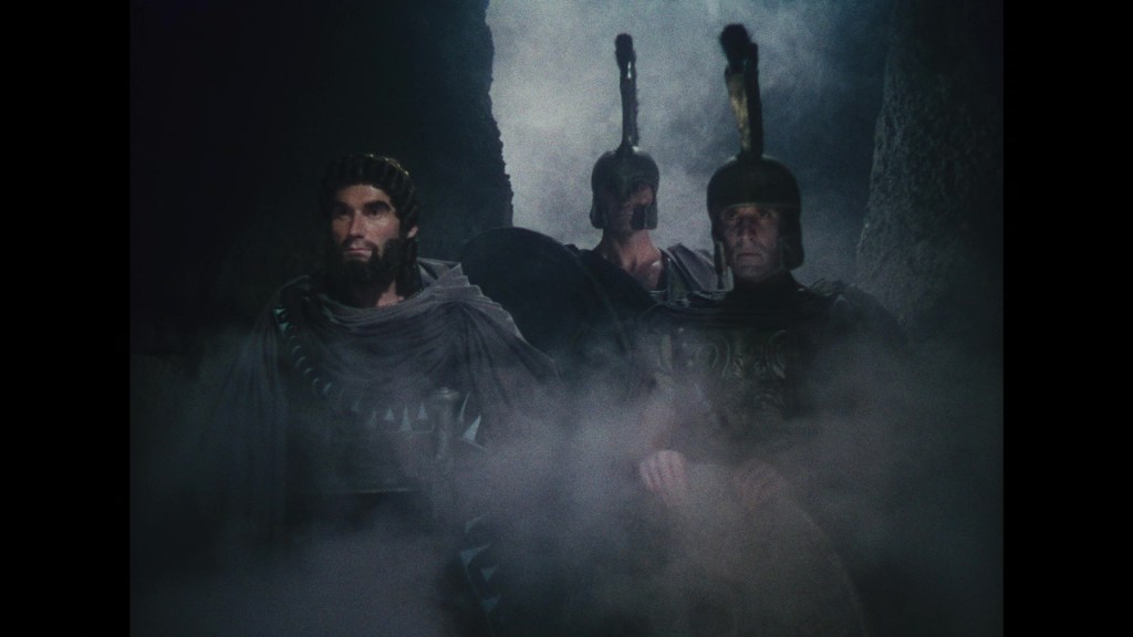 Three ancient warriors in cloaks and armor, standing amidst fog in a dramatic setting.