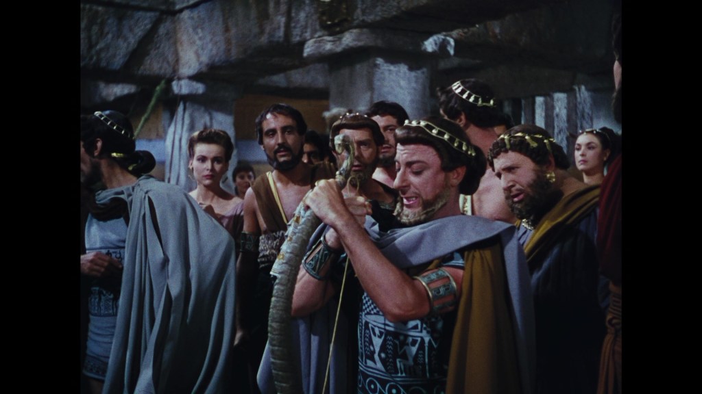 A group of ancient Greek characters in a dramatic scene, with one man holding a sword and engaging the crowd, while others look on with expressions of intrigue and interest.