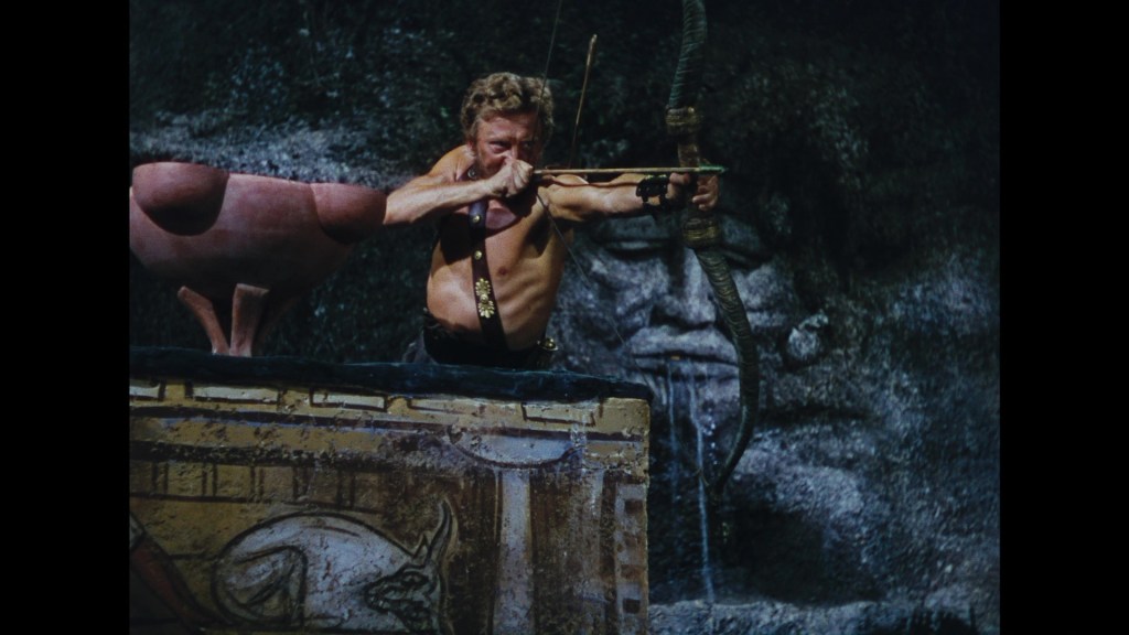 A muscular man with a bow and arrow aiming intently, set against a textured stone backdrop featuring an ancient face and decorative artwork.