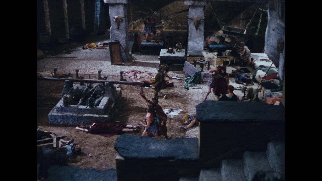 A wide-angle view of a historical setting, depicting a chaotic scene with several characters in tunics, some appearing to be injured or unconscious, scattered around a stone-floored interior resembling an ancient arena or barracks.