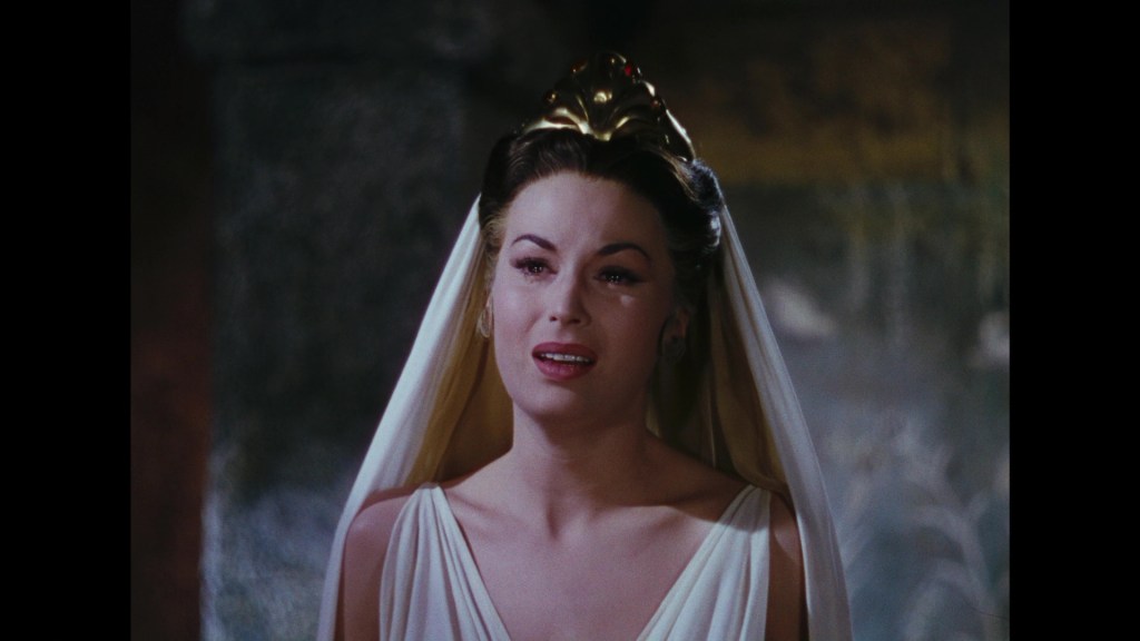 A woman wearing a white dress and a decorative crown, with a veil, looking emotional in a dimly lit setting.