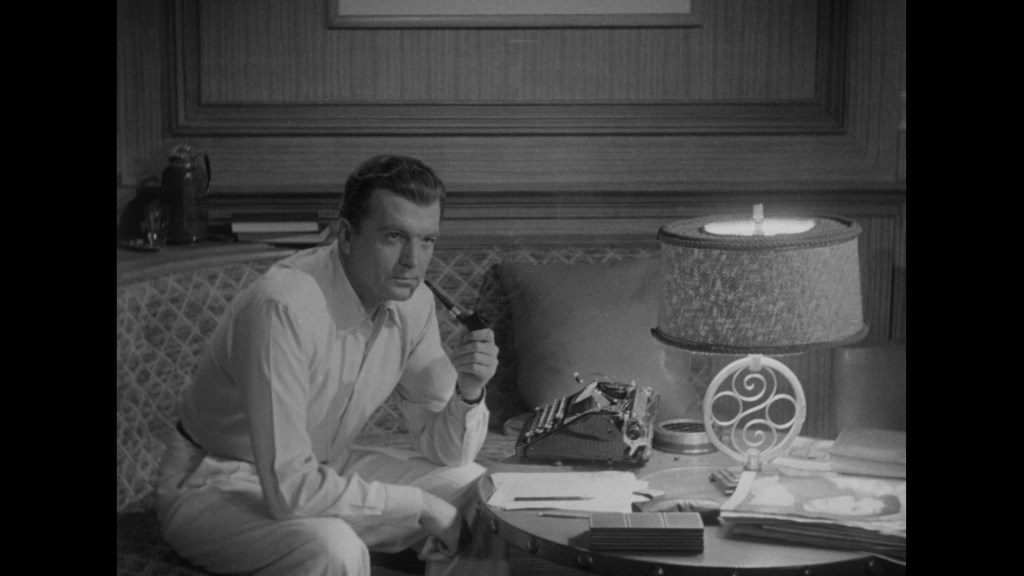 A man sitting on a couch in a stylish room, holding a cigarette with a serious expression. A typewriter and various documents are on the table beside him, with a lamp providing soft lighting.