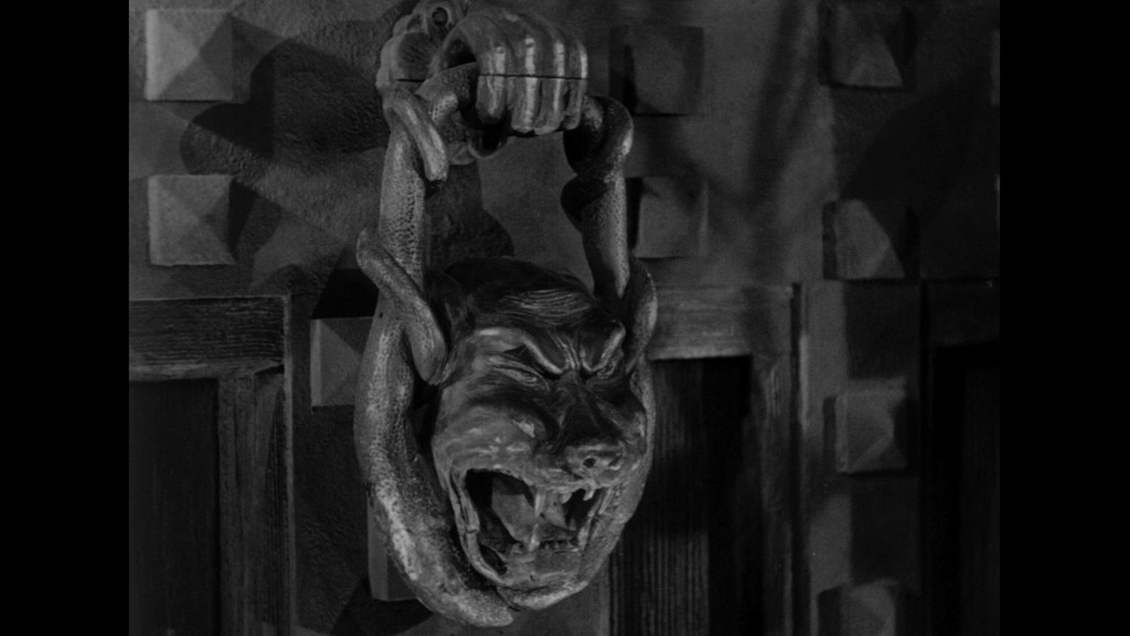 A detailed, vintage door knocker in the shape of a snarling dog's head, attached to a textured wall.