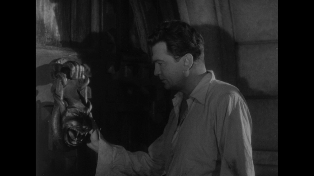 A man in a light-colored shirt is reaching towards a lion-shaped door knocker on a wooden door.