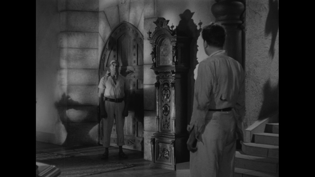 A tense scene in black and white featuring two men facing each other in a dimly lit room, one standing near a large ornate clock and an arched door.