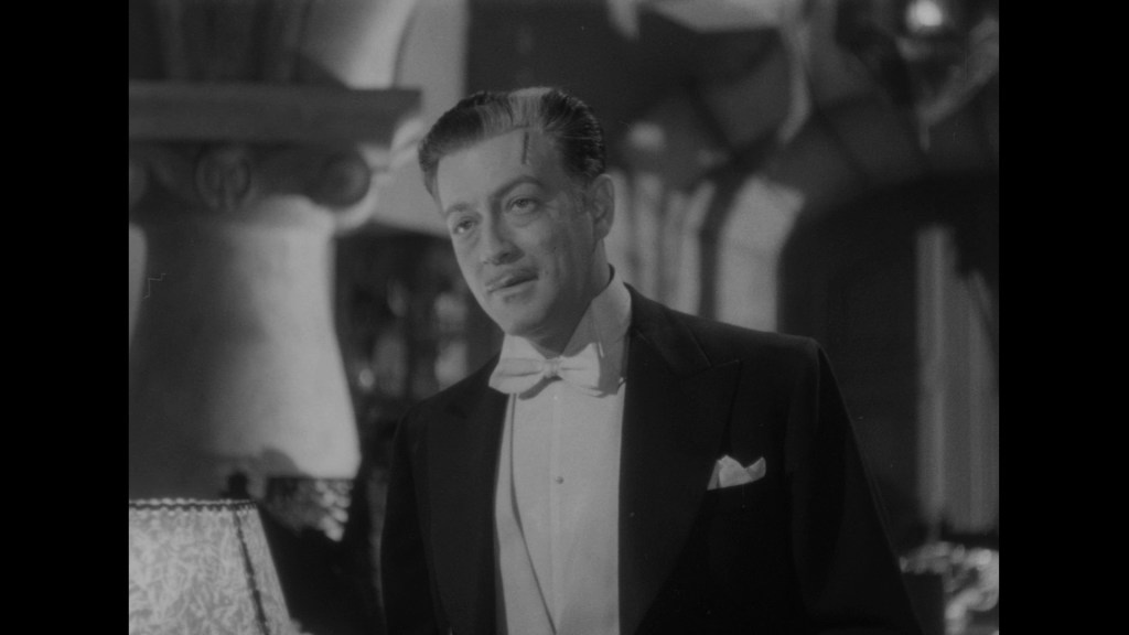 A man in a tuxedo speaking, with a slight smile, in a vintage black and white setting.