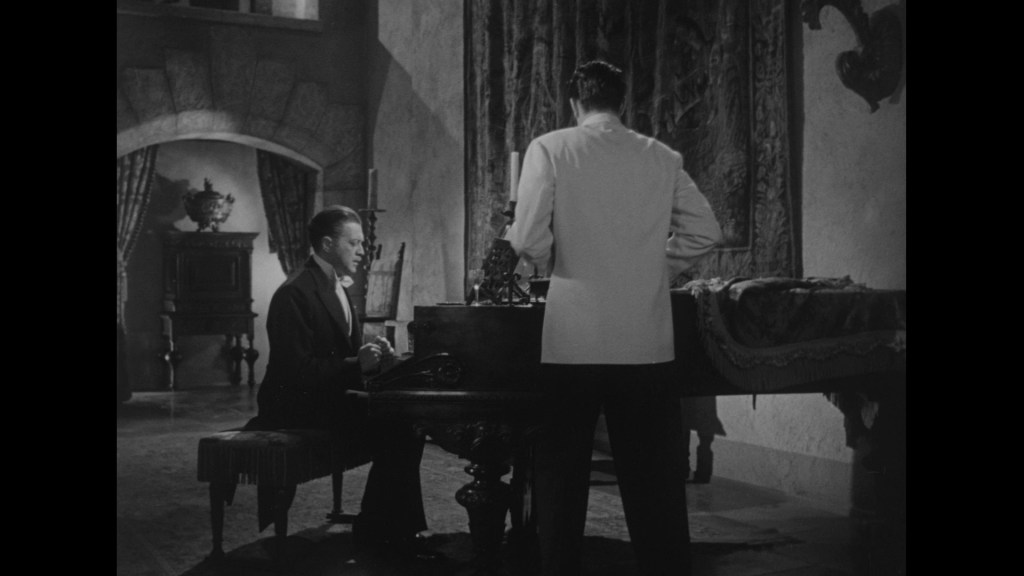A scene from a classic film featuring a man playing the piano while another man stands nearby, both dressed formally in a richly decorated room.