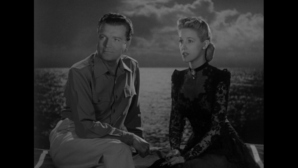 A black and white scene featuring a man in a collared shirt and a woman in an elegant dark dress, sitting by the water under a cloudy sky.