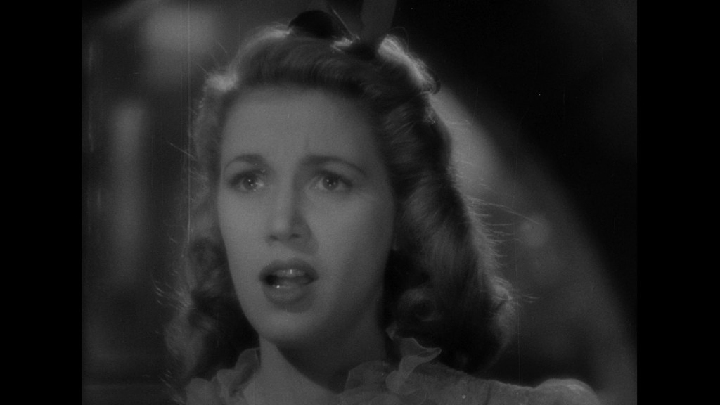 A close-up of a woman with wavy hair, looking surprised or concerned, captured in black and white.