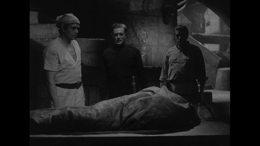 Three men standing over a covered figure on a table in a dimly lit setting, conveying a sense of mystery and tension.
