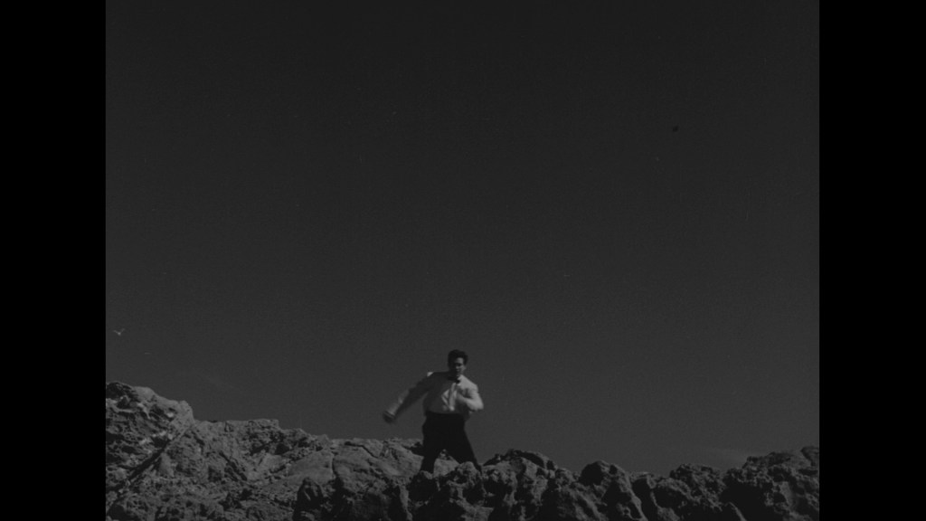 A person in formal attire running on rocky terrain under a clear sky.