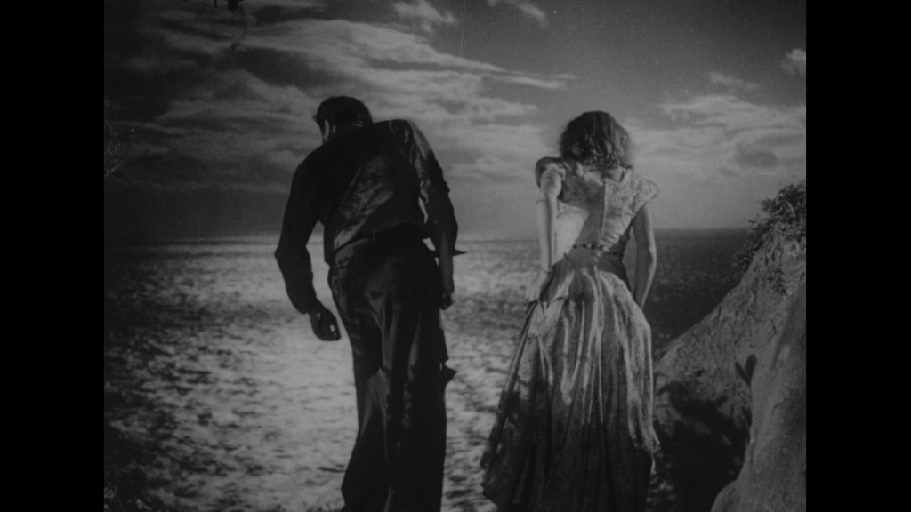 Two figures, a man and a woman, stand on a cliff overlooking a vast ocean, with a dramatic sky overhead. The man is dressed in dark clothing, while the woman wears a vintage dress.