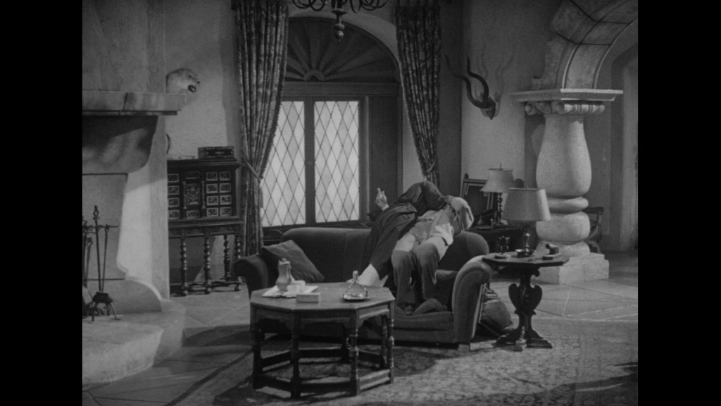 A vintage black-and-white interior scene featuring a cozy living room with a sofa, coffee table, and decorative elements such as curtains and a fireplace.