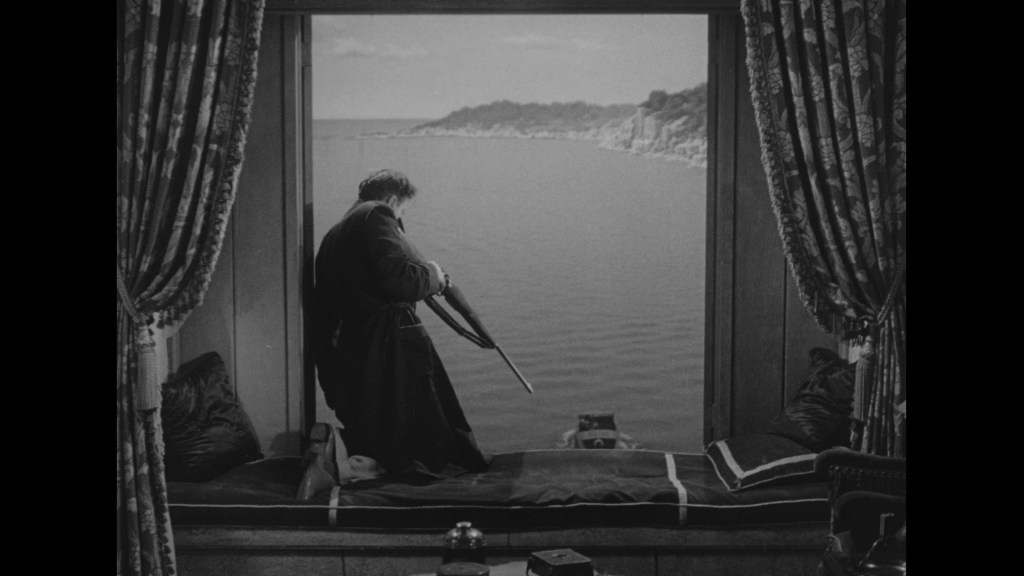 A man standing by a large window, looking out at a body of water, holding an umbrella, with curtains in the foreground.