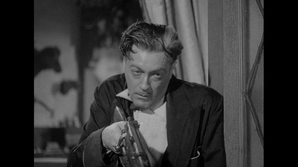 A man in a suit holding a rifle, looking intently off to the side, with a serious expression on his face.